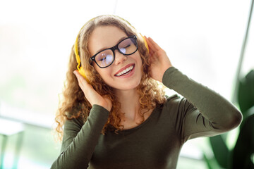 Cheerful woman enjoying music with headphones in a cozy setting, embracing a peaceful moment with a...