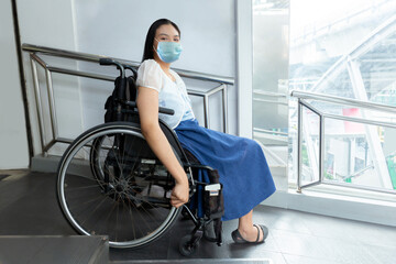 Young asian disabled woman wear protective mask in wheelchair near handicapped walkway, New normal...