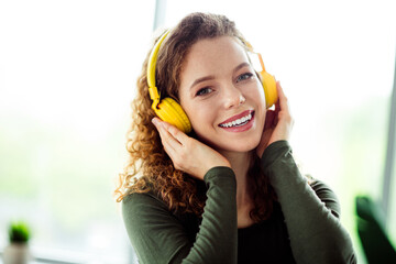 Charming young woman enjoying music with headphones in a comfortable indoor setting, showcasing...
