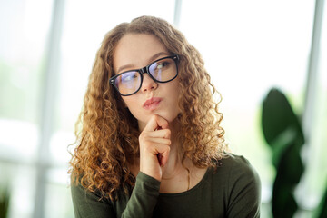 Thoughtful woman in glasses with a thoughtful expression indoors, showcasing stylish casual attire...