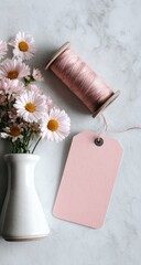 Delicate pink flowers, a spool of thread, and a blank tag on a marble surface