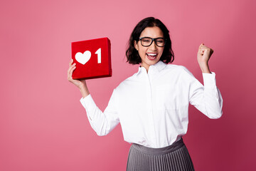 Charming businesswoman celebrating success holding a love sign box on a pink background wearing...