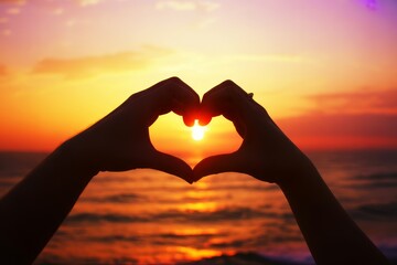 Hands forming heart shape against sunset over ocean