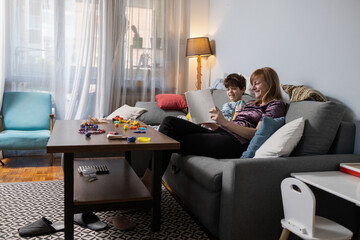 Mother and son relaxing on sofa, reading a book together in cozy living room