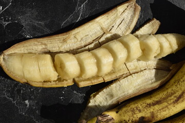 close-up sliced banana in its peel on black cut board top view 