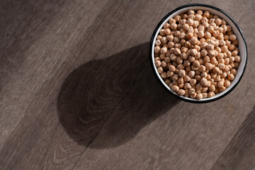 vintage enamel bowl filled with dried chickpeas, the bowl is casting a diagonal shadow across the...
