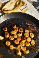 Fried banana slices in caramel on black frying pan on white wooden background. Preparation process