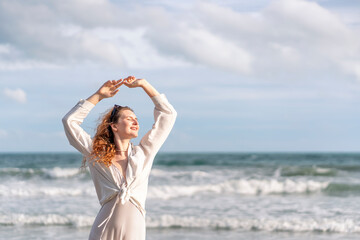 young carefree woman in casual outfit standing at the beach,closed eyes,arms outstretched,relaxing,feeling breeze and freedom,happy caucasian female tourist in seashore on summer vacation