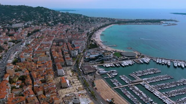 Sweeping drone view of Cannes : La Croisette beach, Palais des Festivals, terracotta rooftops and a packed superyacht harbor on the turquoise Mediterranean.