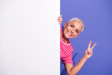 Elderly Woman Wearing a Striped Shirt Smiling and Making a Peace Gesture Against a Purple Background