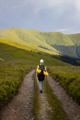 Solo hiker with backpack walking along mountain trail in scenic green landscape. Peaceful nature, travel adventure, and outdoor exploration in summer hills and valleys.