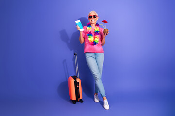 Charming elderly woman in casual attire preparing for vacation with props for leisure against a...