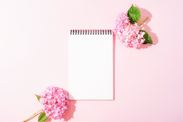 Blank notepad with pink hydrangea flowers on pastel background. Top view, flat lay, mockup