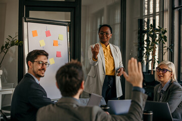 Businesswoman leading a presentation to her colleagues raising their hands to ask questions