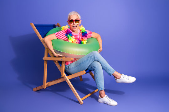 Smiling elderly woman with inflatable float on chair, enjoying leisure on a colorful background