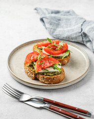 Healthy sesame toast with tomatoes, mozzarella, arugula and pesto on plate on light background