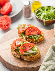 Healthy sesame toast with tomatoes, mozzarella, arugula and pesto on wooden board on light background