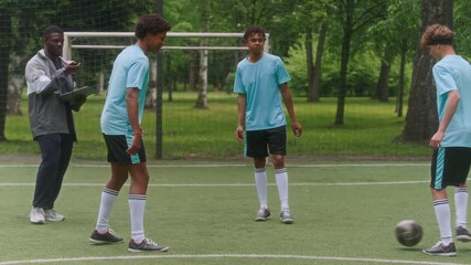 African American male soccer coach and young players standing on grassy field discussing game tactics and strategy after dribbling drill practice in circle - Powered by Adobe