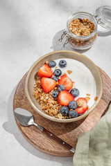 Natural yogurt with granola, blueberry and strawberry in a bowl on a wooden board on a light background