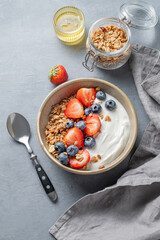 Natural yogurt with granola, blueberry and strawberry in a bowl on a blue background with honey