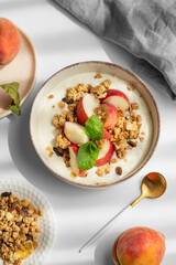 Natural greek yogurt with granola or muesli, peach and mint in a bowl on a white background