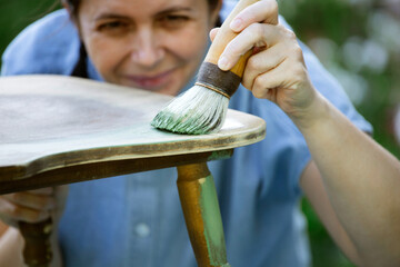 Woman  painting a wooden furniture outdoors, an eco-friendly re-use business.