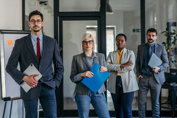 Business team posing in modern office holding documents and digital tablet