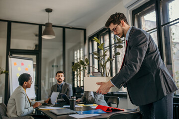 Businessman leaving office after job loss carrying box with belongings