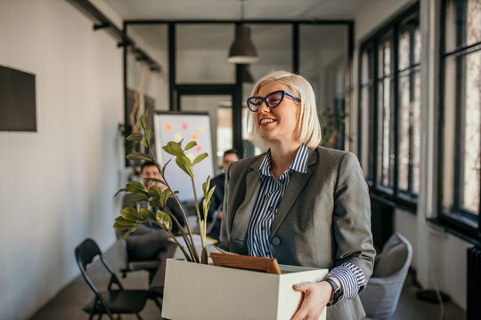 Smiling businesswoman leaving office carrying box with belongings