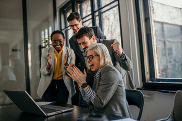 Business team celebrating success looking at laptop in office