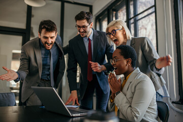Excited business team celebrating success while watching laptop in office