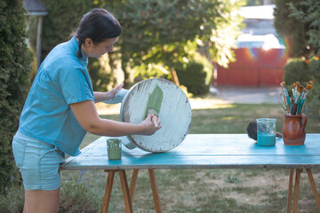 Woman  painting a wooden furniture outdoors, an eco-friendly re-use business.