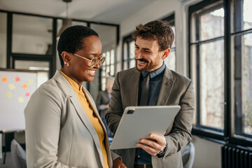 Business colleagues sharing ideas and smiling at digital tablet in office