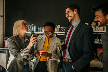 Business people enjoying coffee break and sharing funny content on mobile phone