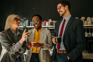 Business people enjoying coffee break and sharing funny content on mobile phone