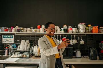 Smiling manager using smartphone in office kitchen during break time