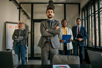 Confident business team standing in modern office with arms crossed and documents ready