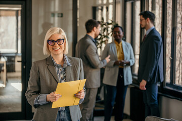 Smiling businesswoman holding folder with colleagues discussing in background