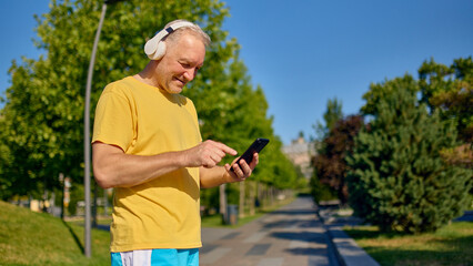 Elderly man interacting with smartphone while enjoying music on morning walk. Concept of senior...