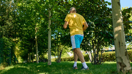 Older man walking through shaded trees during morning exercise. Concept of wellness walk, senior...