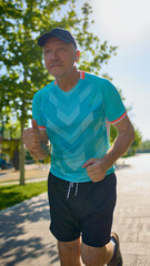 Close-up of older man jogging in blue sportswear with focused expression. Concept of urban fitness, health awareness, mental strength, active aging, sportswear branding.