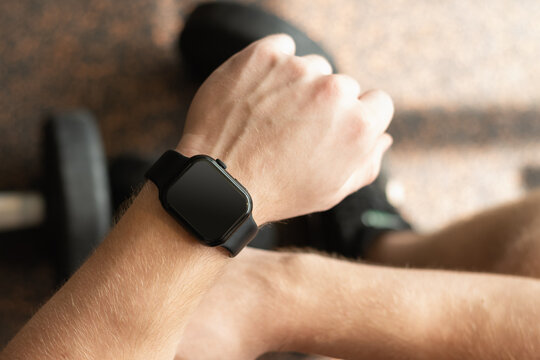 Person in gym with smartwatch on wrist, set against background with gym equipment. Check fitness progress in apps. Mock up.