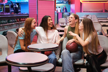 Group of female friends enjoying time together, chatting and laughing while sitting at a table in a bowling alley
