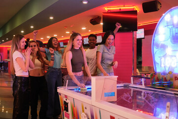 Group of young people having fun playing air hockey together in a colorful amusement arcade