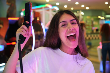 Young woman having fun playing in the arcade, holding a toy gun and screaming