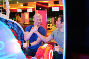 Two male friends shaking hands while having fun and playing arcade game in a bowling alley