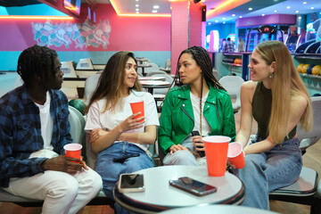 Four friends chatting and having drinks at a bowling alley, enjoying their leisure time together