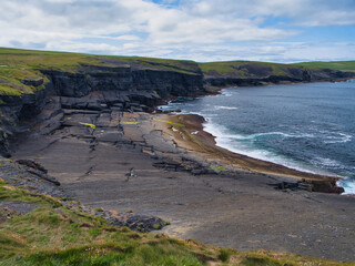 Breathtaking view of Kilkees coastal cliffs, highlighting the striking stratified rock formations against the ocean backdrop under a cloudy sky.