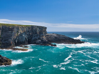 Dramatic cliffs tower over vibrant turquoise waters at Mizen Head, Ireland, under a clear blue sky. The scene captures the raw, natural beauty of the coastline.
