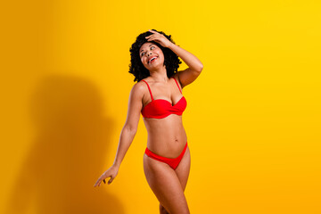 Portrait of a cheerful young woman wearing a red bikini posing joyfully against a bright yellow...